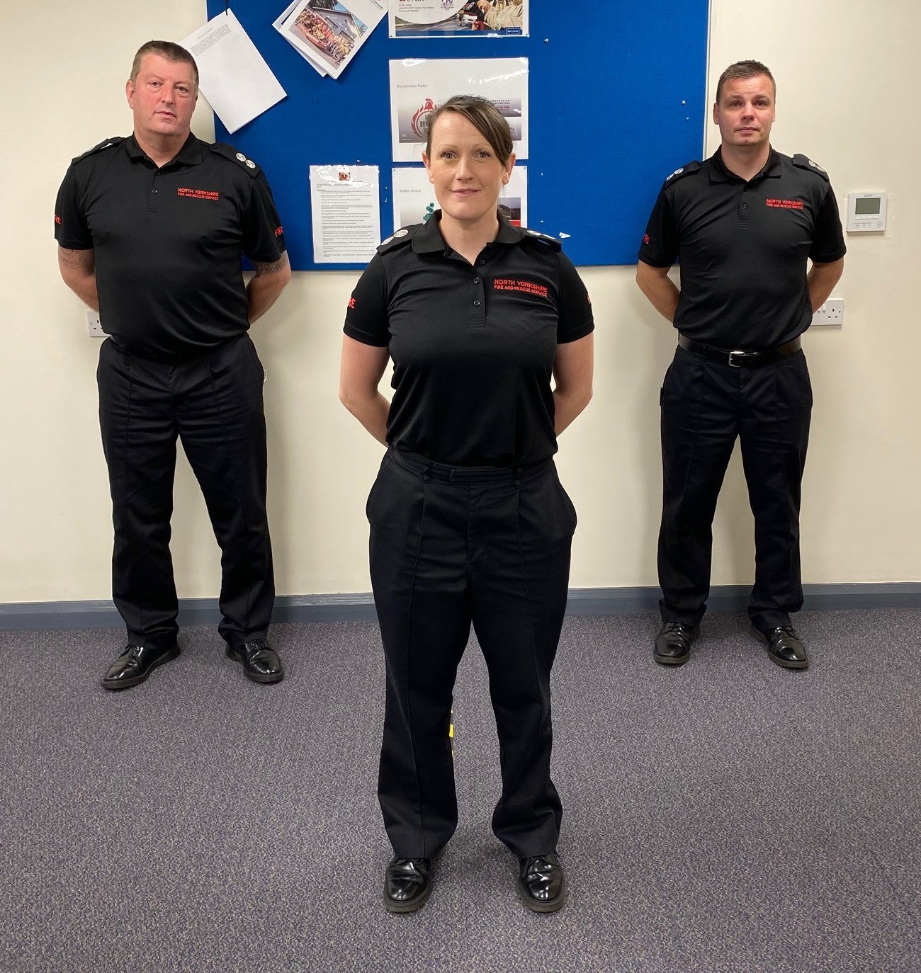 three members of staff stood against a wall showing new tshirts